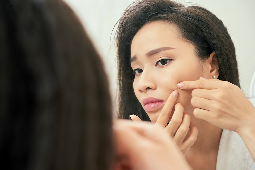 Young woman squeezing pimple in bathroom mirror